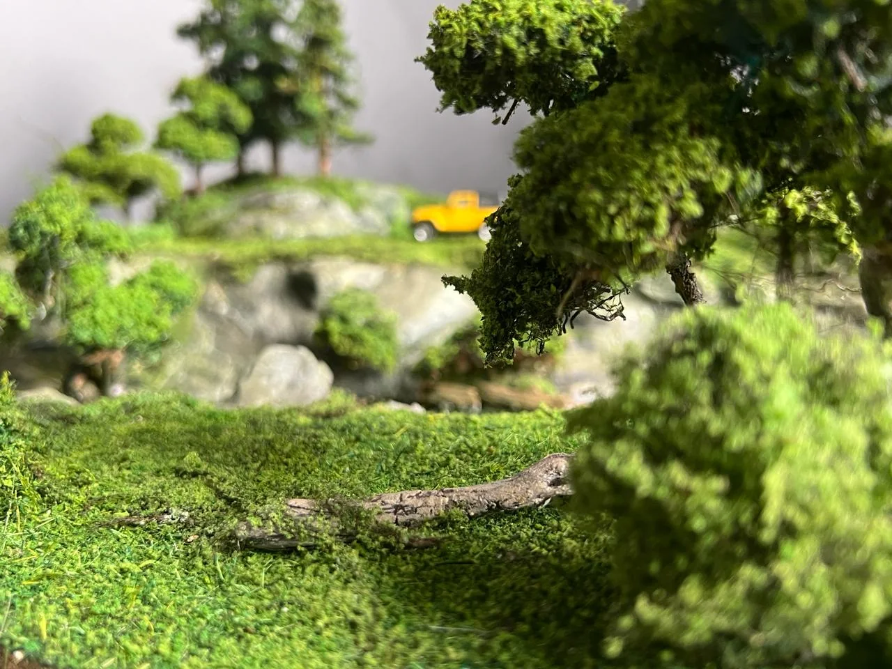 Miniature English countryside terrain with trees and a yellow vehicle.