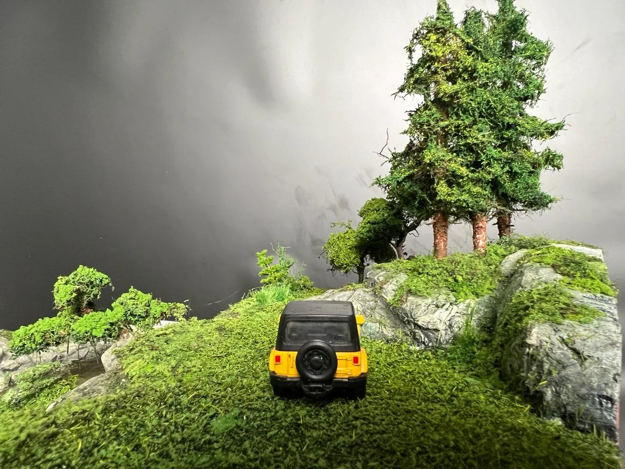 Miniature yellow vehicle approaching a group of pine trees.