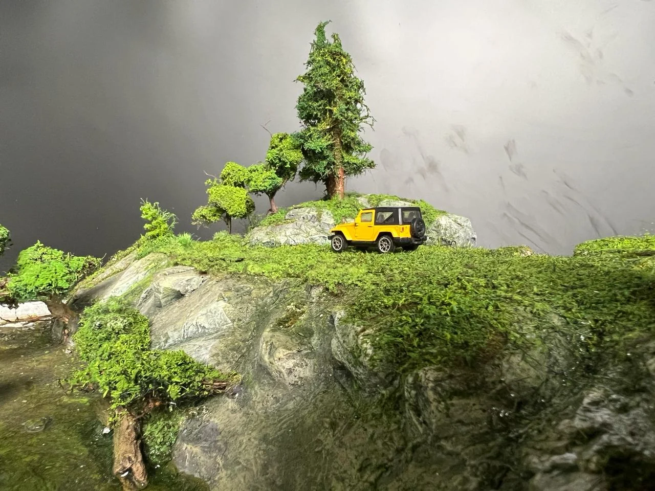 Yellow miniature vehicle positioned on a detailed rocky green ridge.