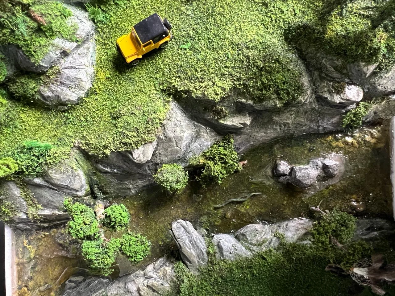 Top-down miniature terrain with rocks, water, and a yellow car.